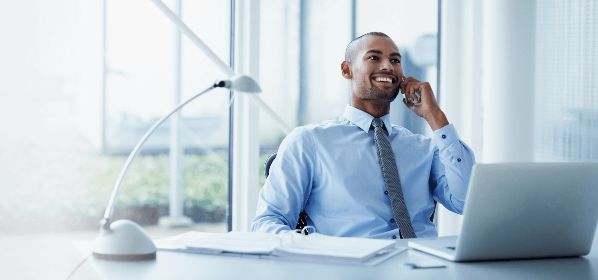 Smiling businessman looking away while using mobile phone at desk in office.